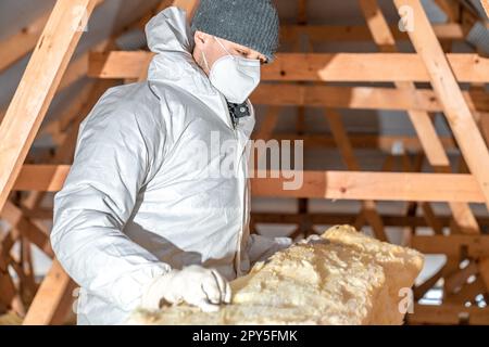 l'uomo isola il tetto e il soffitto della casa con lana di vetro Foto Stock