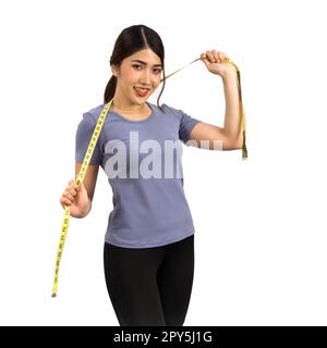 Giovane donna asiatica in abiti da fitness che tiene un metro a nastro con un sorriso. Ritratto su sfondo bianco con luce da studio. Nutrizione sana e concetto di perdita di peso. Foto Stock