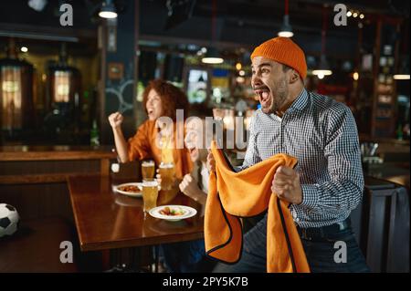 Due ragazzi e una donna al pub che guardano una partita di calcio e bevono birra Foto Stock