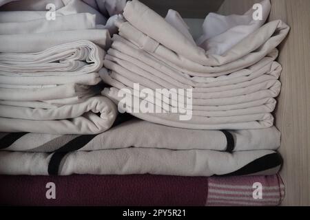 Le lenzuola bianche sono impilate nell'armadio. Contenuto interno di un armadio in lino. Organizzazione familiare. Condizioni igieniche per il sonno. Tessuti e lenzuola in un armadio o guardaroba bianco a metà aperto Foto Stock
