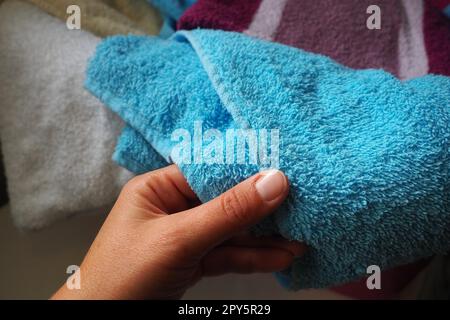 La mano di una donna sente un asciugamano di cotone da un cesto con la biancheria sporca. Smistamento e lavaggio del bucato. Lavanderia o bagno. Servizio di pulizia. Asciugamani di spugna rosa e blu. Foto Stock