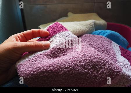 La mano di una donna sente un asciugamano di cotone da un cesto con la biancheria sporca. Smistamento e lavaggio del bucato. Lavanderia o bagno. Servizio di pulizia. Asciugamani di spugna rosa e blu. Foto Stock