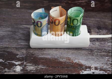 presa tripla con varie banconote in euro su fondo in legno, concetto per l'aumento dei costi energetici Foto Stock