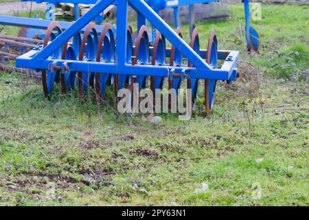 Le attrezzature agricole pesanti blu come l'aratro con dischi in acciaio affilato per la coltivazione agricola su campo con attrezzature trainate da trattore per la preparazione del lavoro sul campo facilitano la meccanizzazione del lavoro agricolo duro Foto Stock