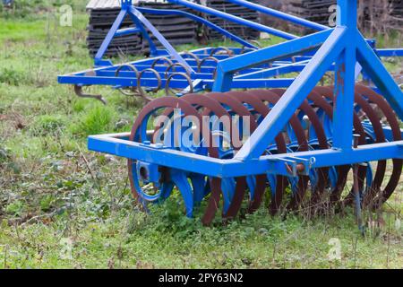 Le attrezzature agricole pesanti blu come l'aratro con dischi in acciaio affilato per la coltivazione agricola su campo con attrezzature trainate da trattore per la preparazione del lavoro sul campo facilitano la meccanizzazione del lavoro agricolo duro Foto Stock