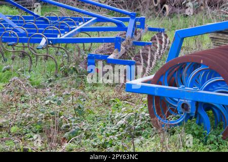 Le attrezzature agricole pesanti blu come l'aratro con dischi in acciaio affilato per la coltivazione agricola su campo con attrezzature trainate da trattore per la preparazione del lavoro sul campo facilitano la meccanizzazione del lavoro agricolo duro Foto Stock