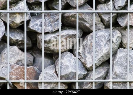 Il bordo delle rocce grezze e le pareti in pietra grigia fanno da sfondo a pietre naturali con materiale frantumato e grezzo impilato nella griglia metallica come massiccio bordo in colori grigi come sfondo minerale naturale per i giardini Foto Stock