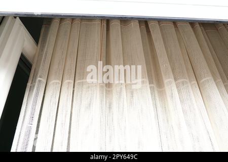 Tende bianche in cotone grossolano o lino fatte di trame di fili sottili. Appartamento interno semplice, compatto ed economico. Decorazione delle finestre in camera. Striscia rossa. Foto Stock