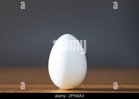 Uovo bianco su fondo grigio al centro su tavola di legno. Design, arte visiva, concetto di minimalismo alimentare Foto Stock