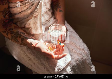 Non è la mattina senza un multivitaminico. una donna che prende una pillola con un bicchiere d'acqua durante la sua routine mattutina a casa. Foto Stock