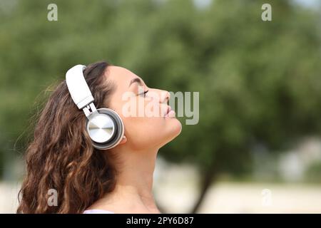 Donna rilassata con cuffie che meditano in un parco Foto Stock