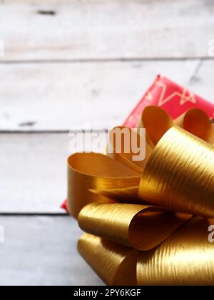 Confezione regalo rossa con un grande arco dorato su sfondo di legno dipinto con vernice bianca. Regalo per Natale, Capodanno, compleanno, festa della mamma, matrimonio, San Valentino. Bella decorazione festiva Foto Stock