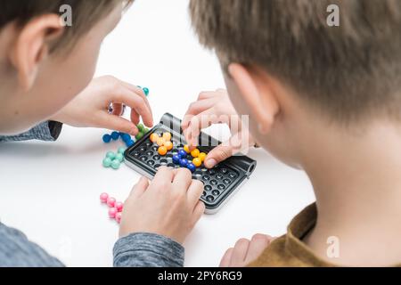 I ragazzi giocano al tavolo tetris sul tavolo, dalla vista delle nuvole. Le mani dei giocatori raccolgono dettagli colorati sul tabellone. Giochi da tavolo. Foto Stock