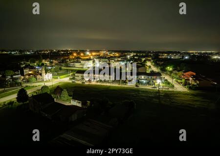 Incantevole vista aerea notturna di un piccolo villaggio italiano immerso nella tranquilla Valle del po, che si illumina sotto il cielo illuminato dalla luna. Foto Stock