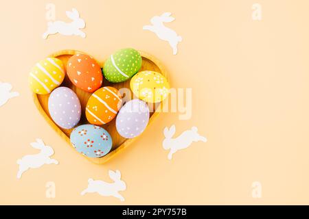 Overhead uova di pasqua con carta di coniglio tagliato in forma di cuore isolato su sfondo pastello Foto Stock