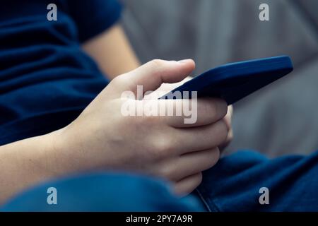 Primo piano mani maschili irriconoscibili che reggono lo smartphone in una custodia blu, seduto sul divano. Attività di marketing commerciale Foto Stock