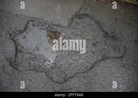 Danni alla strada causati da buche nell'asfalto della carreggiata Foto Stock