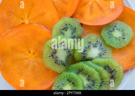 Fresche e mature succose fette di kiwi con persimmon disposti su una piastra, vista dall'alto Foto Stock