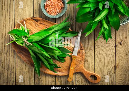 Foglie fresche di porro selvatico su un asse di legno. Foglie di ramson fresco con sale himalayano rosa. Foto Stock