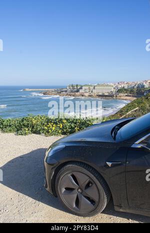 Ericeira, Portogallo - 2 aprile 2023: Costiera panoramica a Eirceira. Vista dalla scogliera. Mare ondulato. Skerries rocciosi. Foto statica di una Tesla modello 3 nera. Foto Stock