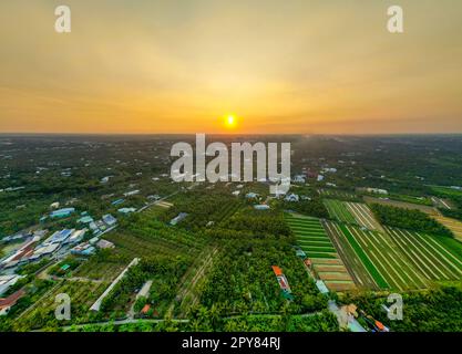 Golden Hour Magic: Tramonto mozzafiato sui campi della provincia di Tien Giang con il fiume sereno e il paesaggio urbano in Vietnam Foto Stock