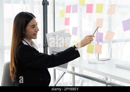 Buone idee per la pianificazione di una donna di affari su una parete di vetro con note appiccicose colorate all'interno di un ufficio Foto Stock