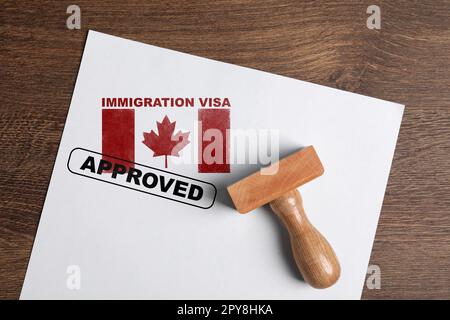 Documento con visto d'immigrazione approvato in Canada e timbro su tavolo di legno, vista dall'alto Foto Stock