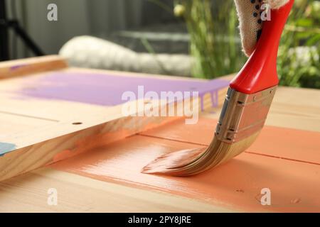 Lavoratore che applica vernice corallo su superficie di legno contro sfondo sfocato, primo piano. Spazio per il testo Foto Stock