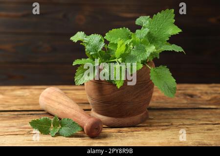 Mortaio con pestello e foglie fresche di limone verde su legno, primo piano Foto Stock