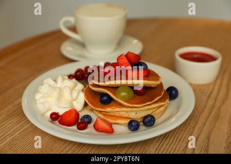 Gustose frittelle con frutti di bosco freschi e panna montata su un tavolo di legno Foto Stock