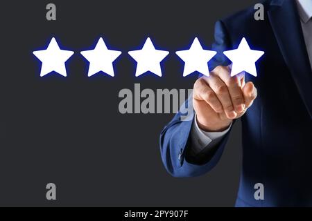 Uomo che indica le icone di cinque stelle su sfondo grigio scuro, primo piano. Valutazione della qualità Foto Stock