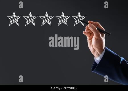 Uomo che indica le icone di cinque stelle su sfondo grigio scuro, primo piano. Valutazione della qualità Foto Stock