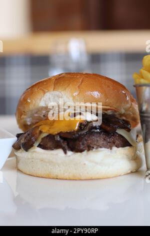 Un hamburger dall'aspetto delizioso con un polpetto di manzo, formaggio fuso, pancetta croccante e un lato di patatine fritte Foto Stock