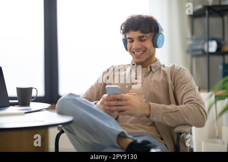 Cheerful Man utilizzando cellulare indossare cuffie ascoltare la musica a casa Foto Stock
