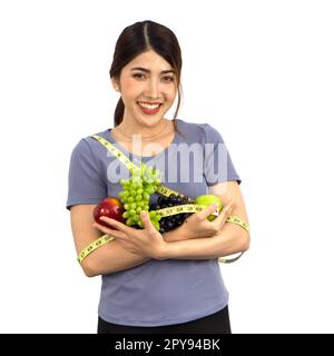 Giovane donna asiatica in abiti per il fitness che tiene la frutta con il metro a nastro. Ritratto su sfondo bianco con luce da studio. Nutrizione sana e concetto di perdita di peso. Foto Stock