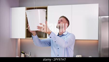 Uomo che tiene la benna mentre goccioline d'acqua fuoriescono dal soffitto Foto Stock