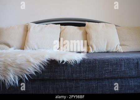 Divano grigio con imbottitura ruvida boucle e cuscini decorativi scanalati bianchi. Un lungo tappeto o copriletto bianco in pelliccia sintetica viene gettato sul sedile. Interno del soggiorno Foto Stock