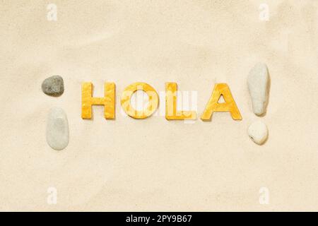 Hola! - Saluto spagnolo con lettere dorate nella sabbia bianca Foto Stock