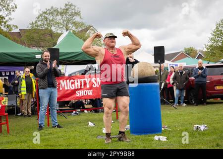 Culcheth, Regno Unito. Lunedì, 1 maggio, 2023, Culcheth, Inghilterra - nonostante i cieli grigi e alcune piovose, Culcheth e Glazebury Community Day sul verde del villaggio che offre intrattenimento da parte del Children’s Entertainer Ian “Zippy” Lees, Northern Stars Dance & Fitness e il Mighty Smith Strongman Show, con sidestalls e luna Park. Adrian Smith flette i suoi muscoli dopo aver sollevato una palla Atlas su un barile di plastica blu credito: John Hopkins/Alamy Live News Foto Stock