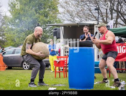 Culcheth, Regno Unito. Lunedì, 1 maggio, 2023, Culcheth, Inghilterra - nonostante i cieli grigi e alcune piovose, Culcheth e Glazebury Community Day sul verde del villaggio che offre intrattenimento da parte del Children’s Entertainer Ian “Zippy” Lees, Northern Stars Dance & Fitness e il Mighty Smith Strongman Show, con sidestalls e luna Park. Adrian Smith incoraggia un membro del pubblico a sollevare un Atlas Stone Credit: John Hopkins/Alamy Live News Foto Stock