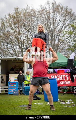 Culcheth, Regno Unito. Lunedì, 1 maggio, 2023, Culcheth, Inghilterra - nonostante i cieli grigi e alcune piovose, Culcheth e Glazebury Community Day sul verde del villaggio che offre intrattenimento da parte del Children’s Entertainer Ian “Zippy” Lees, Northern Stars Dance & Fitness e il Mighty Smith Strongman Show, con sidestalls e luna Park. Adrian Smith tiene una signora su una sedia sopra la testa con i suoi denti credito: John Hopkins/Alamy Live News Foto Stock