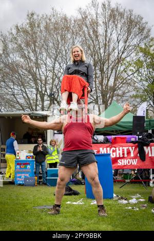 Culcheth, Regno Unito. Lunedì, 1 maggio, 2023, Culcheth, Inghilterra - nonostante i cieli grigi e alcune piovose, Culcheth e Glazebury Community Day sul verde del villaggio che offre intrattenimento da parte del Children’s Entertainer Ian “Zippy” Lees, Northern Stars Dance & Fitness e il Mighty Smith Strongman Show, con sidestalls e luna Park. Adrian Smith tiene una signora su una sedia sopra la testa con i suoi denti credito: John Hopkins/Alamy Live News Foto Stock