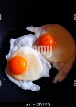 Due uova di pollo fritte in una padella nera da vicino Foto Stock