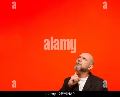 Ritratto di un elegante uomo d'affari che guarda in alto. Isolato su sfondo arancione. Foto Stock