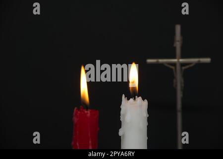 Due candele ardenti e croce cristiana nell'oscurità Foto Stock