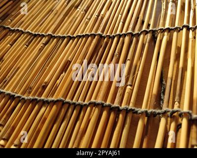 Una biancheria da letto in paglia, una tovaglia o un piccolo tappeto appoggiato su un tavolo e fotografato lateralmente. La luce del sole della sera si riflette sui gambi. Alcuni bastoncini sono rotti, fili e funi sono intrecciati Foto Stock