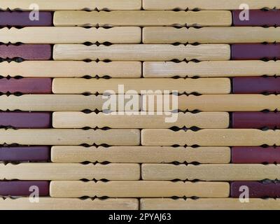 tappetino in legno o lamellare. Il tappeto è un tappetino sotto il caldo. Bastoncini di legno lavorato a maglia con bordi arrotondati. Primo piano. Colori giallo, marrone e beige. Illuminazione laterale. Consistenza tradizionale del tampone di bambù. Foto Stock