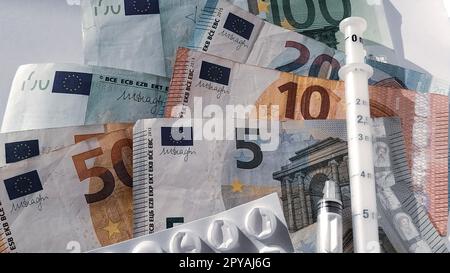 Banconote in euro. Primo piano della moneta europea su sfondo bianco. Confezione bianca con pillole e una siringa di misurazione accanto al denaro. L'alto costo del trattamento. Banconote da 5, 10, 20, 50, 100 euro Foto Stock