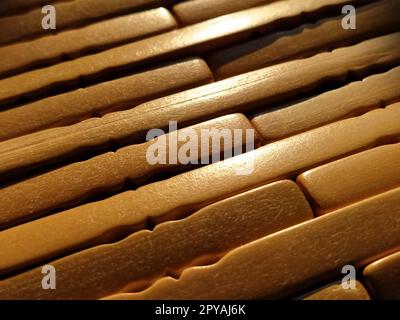 tappetino in legno o lamellare. Il tappeto è un tappetino sotto il caldo. Bastoncini di legno lavorato a maglia con bordi arrotondati. Primo piano. Colori giallo, marrone e beige. Illuminazione laterale. Consistenza tradizionale del tampone di bambù Foto Stock