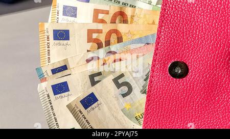 Banconote in euro. Moneta europea su sfondo bianco. Una borsa o una borsa di colore rosa brillante con un bottone di metallo, da cui il denaro viene distribuito in un ventilatore. Banconote da 5, 10, 20, 50 e 100 Foto Stock